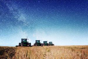 tractor arando el campo agrícola en preparación para la siembra de primavera. fantástico cielo estrellado y la vía láctea foto