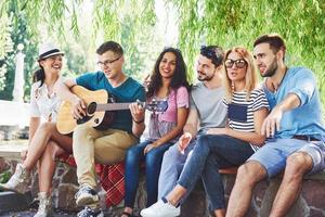 grupo de amigos felices con guitarra. mientras uno de ellos toca la guitarra y otros le dan un aplauso foto