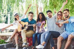 grupo de amigos felices con guitarra. mientras uno de ellos toca la guitarra y otros le dan un aplauso foto