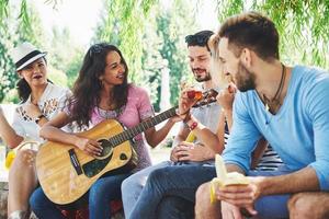 grupo de amigos felices con guitarra. mientras uno de ellos toca la guitarra y otros le dan un aplauso foto