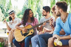 grupo de amigos felices con guitarra. mientras uno de ellos toca la guitarra y otros le dan un aplauso foto