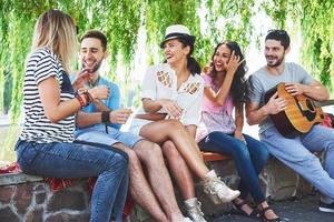 Group of happy friends with guitar. While one of them is playing guitar and others are giving him a round of applause photo