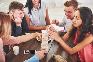 Group of creative friends sitting at wooden table. People having fun while playing board game photo