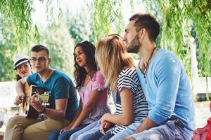 Group of happy friends with guitar. While one of them is playing guitar and others are giving him a round of applause photo