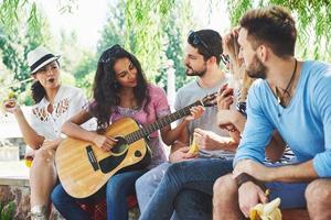 grupo de amigos felices con guitarra. mientras uno de ellos toca la guitarra y otros le dan un aplauso foto