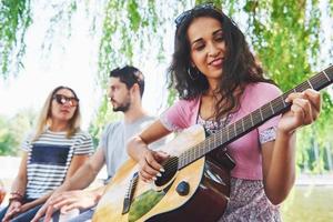 grupo de amigos felices con guitarra. mientras uno de ellos toca la guitarra y otros le dan un aplauso foto