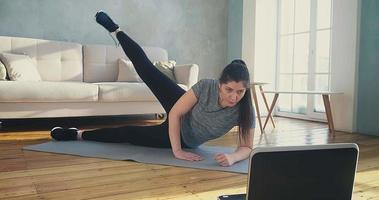 Attentive woman with loose shoelace does supine side leg raises at online training in living room slow motion video