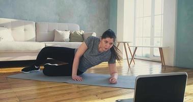 Attentive woman with loose shoelace in sportswear does supine side leg raises at online training in living room slow motion video