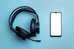 maqueta de teléfono inteligente y auriculares inalámbricos en un escritorio azul limpio. teléfono con pantalla en blanco aislada para la presentación de la aplicación. vista superior, composición plana de primer plano foto