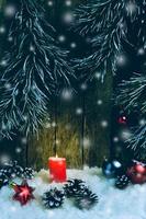 Christmas ornament, red candle and toys in the snow on a wooden background and tree branches