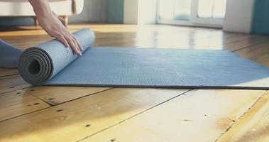 lady yoga trainer en chaussettes déroule un tapis en caoutchouc gris sur parquet avant la leçon de formation dans la chambre le matin en gros plan au ralenti video