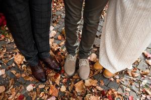 pies de la novia y el novio, así como de su hijo en el fondo de las hojas de otoño