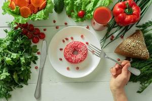 A delicious donut lies on a plate and eats to eat it. Problems of proper nutrition and the concept of choosing between wholesome and not wholesome food photo