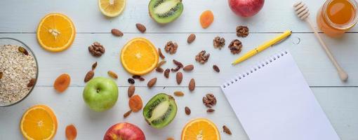 Notebook with pen surrounded by apples, kiwi, dried fruits, oranges and apples. The concept of a healthy diet and shopping list. photo