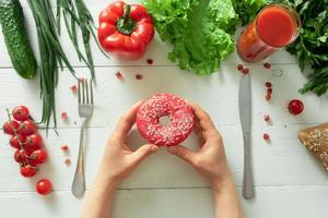 Female hands hold a tasty donut on a background of vegetables. The temptation of dieting photo
