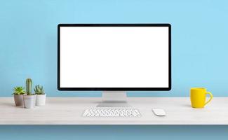 Computer display with white isolated screen for presentation on work desk. Clean composition with coffee mug and plants. Blue wall in background photo