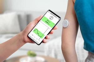 Measurement of blood glucose with the help of mobile app and sensor. Hand brings the phone closer to the sensor located on the child's hand concept photo