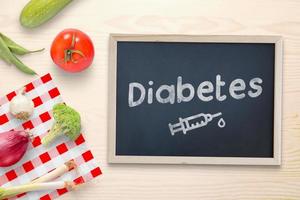 Diabetes written on a chalkboard with a drawing of an insulin injection, in addition to healthy food, vegetables. Top view, flat lay composition photo