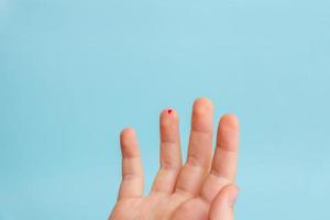 Drop of blood on a child's finger. The concept of measuring blood sugar levels with the help of strips. Blue background photo