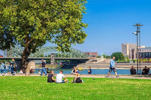 Cologne, Germany, August 23, 2019 people tourists walking down and having a rest on green grass lawn near Rhine river in Cologne photo