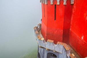red defense wall and tower with merlons of Pena Palace with green forest in fog background, Palacio Nacional da Pena photo