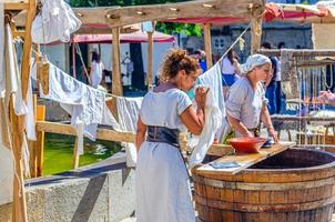 mistress checking maid washing linen, servant woman in old traditional clothes near wooden barrel in historical centre photo