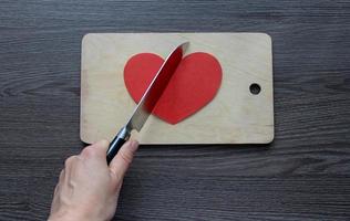 hand with a knife cutting a paper heart on a cutting board photo