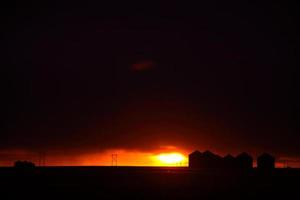 puesta de sol detrás de graneros de metal en saskatchewan foto