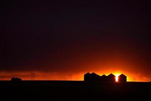 Sun setting behind metal granaries in Saskatchewan photo