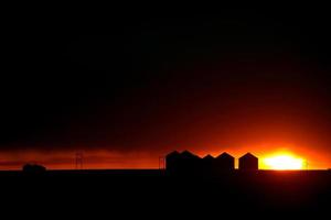 puesta de sol detrás de graneros de metal en saskatchewan foto