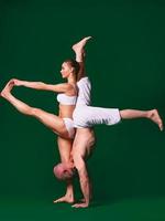 Beautiful sporty woman and man in white clothes doing yoga asanas together indoor on green background photo