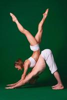 Beautiful sporty woman and man in white clothes doing yoga asanas together indoor on green background photo