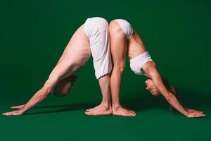 Beautiful sporty woman and man in white clothes doing yoga asanas together indoor on green background photo