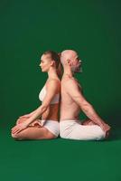 hermosa mujer deportiva y hombre con ropa blanca haciendo asanas de yoga juntos en interiores con fondo verde foto