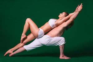 Beautiful sporty woman and man in white clothes doing yoga asanas together indoor on green background photo