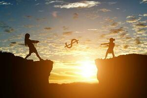 Silhouette of girl pull the rope a dollar coin on cliff at sunset background. Tug of war money hunt concept. photo