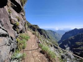 Hiking trail on a beautiful sunny day. Rail for security. Amazing mountain path. Vibrant colors. Travel the world and discover its wonders. Madeira Island, Portugal. photo