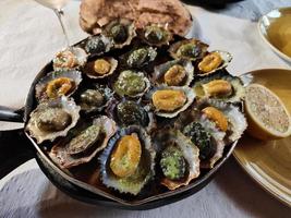 Closeup of tasty limpets with butter sauce served on the hot pan, just freshly made. Lemon on the side. Seafood. Traditional limpets, lapas from Madeira Island, Portugal. Enjoy the food. photo