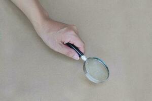 Hand holding a magnifying glass with brown paper background. photo