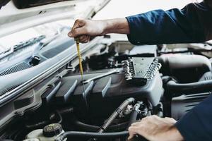 el reparador de automóviles está comprobando el nivel de aceite del motor en el taller automotriz, la inspección de los trabajadores del automóvil de mantenimiento revisa los motores de los vehículos de aceite mediante la prueba de la varilla en la estación de la tienda de automóviles. servicios de automóviles foto