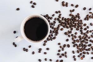 taza de café y granos de café tostados sobre fondo blanco aislado, cierre de ingredientes de café de grano con fondos de taza de café caliente. foto