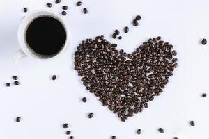 taza de café y granos de café tostados en forma de corazón sobre fondo blanco aislado. primer plano de ingredientes de café de grano con fondos de taza de café caliente. conceptos de comida y bebida foto