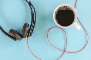 descanso para tomar café y concepto de estilo de vida laboral, taza de café y auriculares en un fondo azul aislado. accesorio de dispositivo de auriculares electrónicos foto