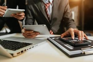 Business documents on office table with smart phone and calculator digital tablet and graph business with social network diagram and two colleagues discussing data working in the office photo