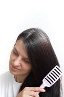 A young woman with gray hair combs her hair. Early gray hair concept, vertical photo