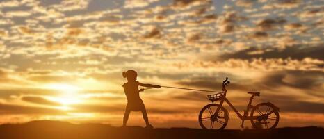 silueta de niña tirando de bicicleta al fondo de la puesta del sol