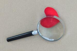 Magnifying glass with heart on brown paper background. Concept of search for LOVE. photo