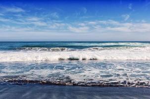 gran ola oceánica rompiendo en una playa de arena negra en el océano pacífico foto