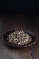 Boiled buckwheat porridge in a clay plate on a wooden background. photo
