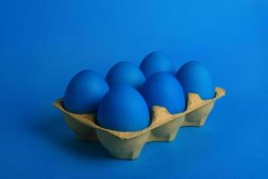 Six blue painted Easter eggs in yellow wrapping on blue background. Happy Easter holiday card or banner.